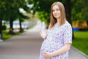 Pregnant woman stands in the park with a bottle of water. copy space photo