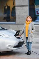 Connecting the Charger Plug of an Electric Car. Girl stands near her electric car and waits when vehicle will charged. photo