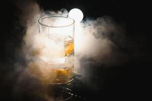 whiskey with ice on black background with smoke photo