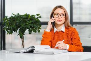 Happy smiling business woman at work talking on phone, sitting at her working place in office, copy space photo