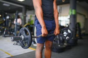 retrato de atlético hombre con barra con pesas en manos hacer ejercicio a gimnasio foto