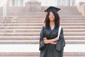 cheerful afro american female graduate standing in front of university building photo