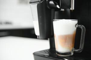 Modern coffee machine with glass cup of latte on white marble countertop in kitchen photo