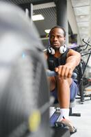 motivado joven negro deportista teniendo rutina de ejercicio en remo máquina foto