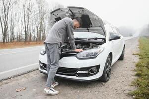 triste hombre en el la carretera siguiente a el roto coche foto