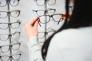 Row of glasses at an opticians. Eyeglasses shop. Stand with glasses in the store of optics. Woman's hand chooses spectacles. Eyesight correction photo