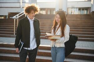 Student couple talking outdoors, holding books, notes and other learning materials photo