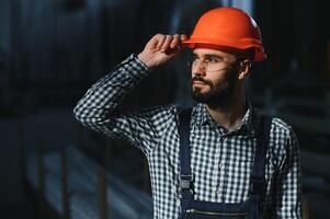 retrato de industrial ingeniero. fábrica trabajador con difícil sombrero en pie en fábrica. foto