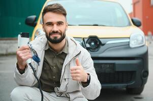 Portrait of a young man standing with charging cable near the charging station photo