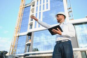 Engineer next to building cranes. Concept - large construction project. Architect directs the construction process. Drawings and tablet in the hands. photo