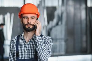 Portrait of Professional Heavy Industry Engineer Worker Wearing Safety Uniform, Hard Hat Smiling. In the Background Unfocused Large Industrial Factory. photo