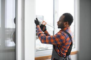 Workman in overalls installing or adjusting plastic windows in the living room at home photo