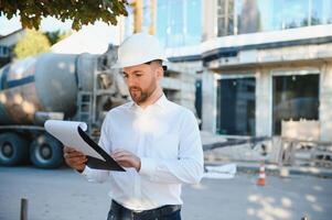Engineer next to building cranes. Concept - large construction project. Architect directs the construction process. Drawings and tablet in the hands. photo