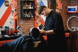 africano masculino cliente consiguiendo Corte de pelo a Barbero tienda desde profesional estilista. foto