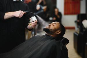 africano masculino cliente consiguiendo Corte de pelo a Barbero tienda desde profesional estilista. foto