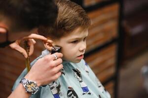 Side view of cute little boy getting haircut by hairdresser at the barbershop. photo