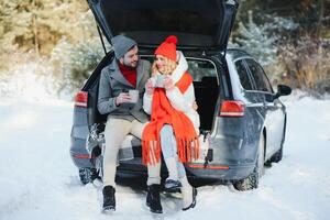 Cute Couple Having Winter Forest Picnic Drinking Tea from Tea Take Away Cup. Nature Picnic. Love Story Date at Car. photo