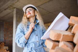 Construction concept. Pretty female builder in overalls and helmet working on construction site. photo