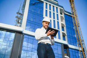 Engineer next to building cranes. Concept - large construction project. Architect directs the construction process. Drawings and tablet in the hands. photo