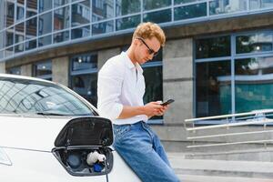 Man with smartphone after finishing charging of battery. Male near electric vehicle photo