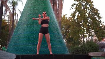 a woman in a black top and shorts is warming up, standing next to a fountain video