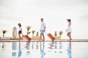 young family with suitcases walking to hotel building with beautiful swimming pool. traveling and relaxing time concept. photo