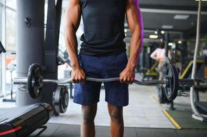 retrato de atlético hombre con barra con pesas en manos hacer ejercicio a gimnasio foto