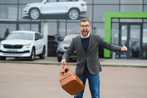 contento comprador cerca el coche en frente de el moderno avtosalon edificio foto