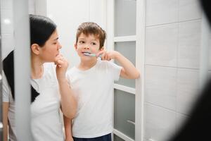 hermosa madre y contento hijo cepillado dientes cerca espejo en baño foto