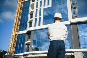 Engineer next to building cranes. Concept - large construction project. Architect directs the construction process. Drawings and tablet in the hands. photo