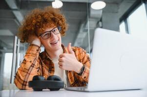 Portrait of cheerful millennial blogger with modern cellphone and laptop technology enjoying freelance lifestyle, happy hipster guy in optical eyewear using mobile phone and netbook in street cafe. photo