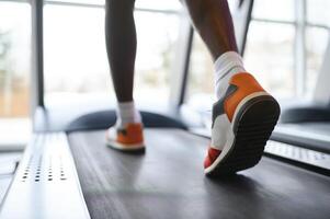 Back view of unrecognizable male legs running on treadmill in gym. photo