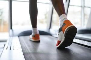 Back view of unrecognizable male legs running on treadmill in gym. photo