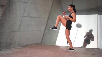 a woman in a black exercising suit doing warm up exercises near mirror wall outdoors city street video