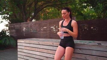 uma mulher dentro Preto calção e uma Esportes sutiã é bebendo água video