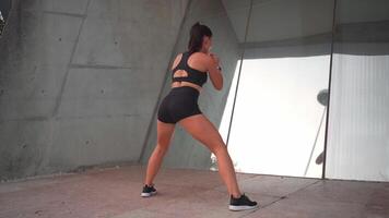 uma mulher dentro uma Preto exercício terno fazendo caloroso acima exercícios perto espelho parede ao ar livre cidade rua video