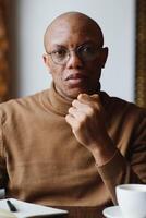 Portrait of smiling African American man in glasses sit at desk in office working on laptop, happy biracial male worker look at camera posing, busy using modern computer gadget at workplace. photo