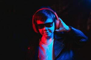 teen boy listening to music with headphones, neon light trending portrait. Looks at the camera photo