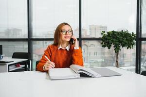 Portrait of happy lady typing in mobile while locating at desk in office photo