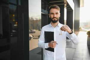 Real estate agent holding key on blurred background, closeup photo