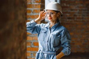 Construction concept. Pretty female builder in overalls and helmet working on construction site. photo