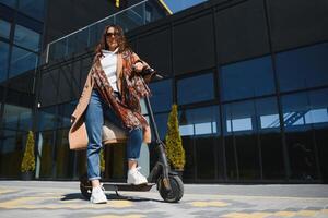 Young beautiful woman riding an electric scooter to work, modern girl, new generation, electric transport, ecology, ecological transport, sunset, electric skateboard. photo