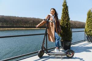 Young beautiful woman riding an electric scooter to work, modern girl, new generation, electric transport, ecology, ecological transport, sunset, electric skateboard. photo