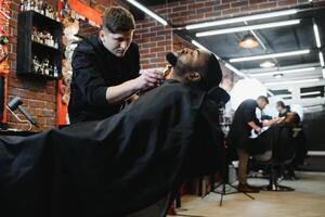 un Barbero es yendo mediante el eléctrico corte y afeitado máquina para el barba de un afroamericano brasileño chico. foto