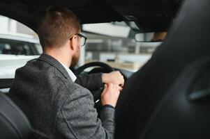 Handsome businessman driving car to airport, going on business side view, copy space. Happy man in stylish suit going to business meeting in the morning, driving his luxury car, shot from cabin. photo