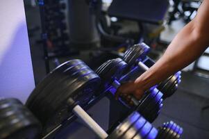 Close-up man grabs a heavy dumbbell in gym with his hand. Concept lifting, fitness photo