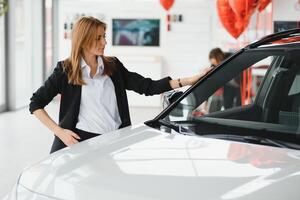joven hermosa mujer demostración su amor a un coche en un coche sala de exposición. foto