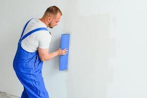 A general laborer in overalls uses a trowel to cover the wall with cement photo