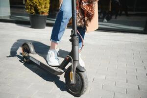 Close up of woman riding black electric kick scooter at cityscape, motion blur photo