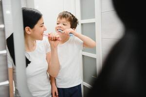 hermosa madre y contento hijo cepillado dientes cerca espejo en baño foto